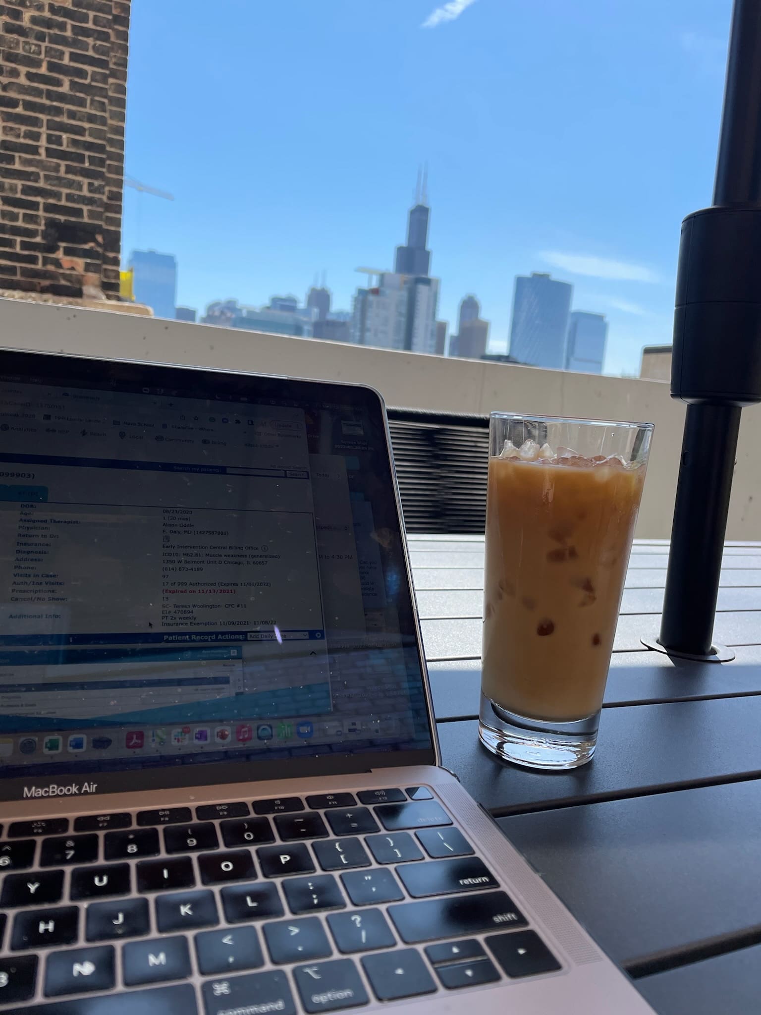 Laptop open on an outdoor table with an iced coffee, overlooking the Chicago skyline on a sunny day.