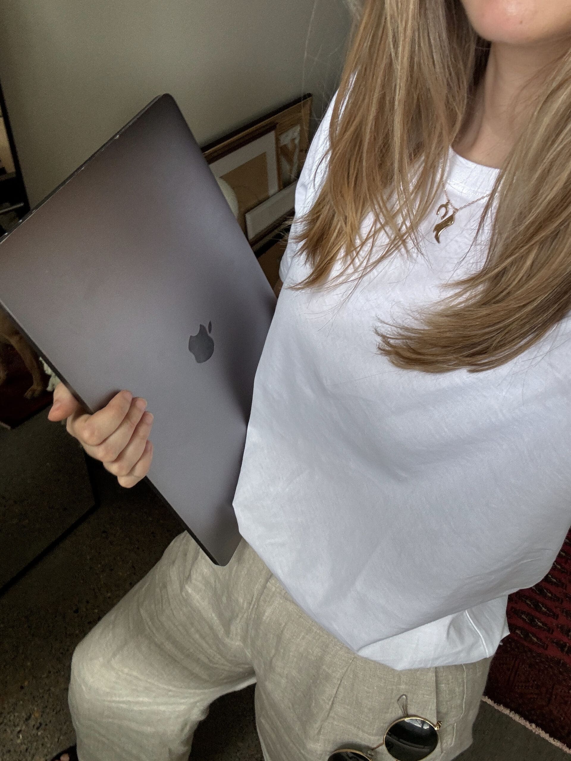 A woman holding a MacBook laptop, dressed in a relaxed business casual outfit, symbolizing productivity and work-life balance.